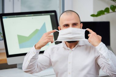 Koronavirüse karşı tıbbi koruyucu yüz maskesi takan bir adam. Çalışma alanında bilgisayarları ve arka planda yeşil bitkileri olan bir ofis çalışanı. 2019-NCoV karantinası.