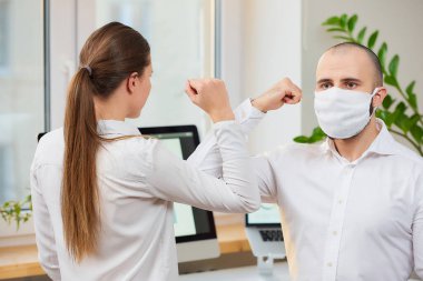 Coronavirus 'un (COVID-19) yayılmasını önlemek için dirsek seği selamı. Tıbbi maskeli bir adam ve bir kız ofiste çıplak elle buluşuyorlar. Sarılmak ya da tokalaşmak yerine, dirseklerini vururlar.