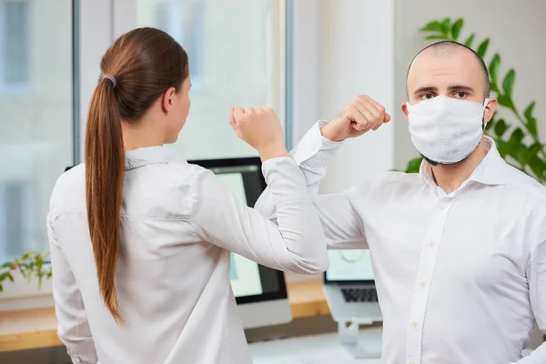 Elbow greeting to avoid the spread of coronavirus (COVID-19). Man with a medical face mask and woman meet in an office with bare hands. Instead of greeting with a hug or handshake, they bump elbows