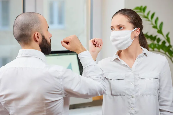 Elbow greeting to avoid the spread of coronavirus (2019-nCoV). Girl with a medical face mask and man meet in an office with bare hands. Instead of greeting with a hug or handshake, they bump elbows