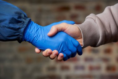 El sıkışalım. Coronavirus 'un (COVID-19) yayılmasını önlemek için tek kullanımlık tıbbi eldivenle bir erkekle el sıkışan bir kadın. İki arkadaş bir sokakta buluşur..