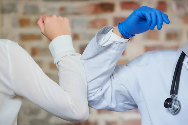 Elbow bumping. A new way of greeting to avoid the spread of coronavirus (COVID-19). A doctor and a female patient bump elbows Instead of greeting with a hug or handshake against a brick wall.