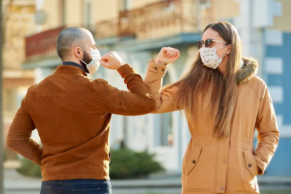 Elbow greeting to avoid the spread of coronavirus (COVID-19). A man and a woman in medical face masks meet on the street with bare hands. Instead of greeting with a hug or handshake, they bump elbows.