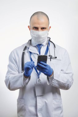 Koruyucu yüz maskesi takmış, akıllı telefon tutan bulaşıcı bir doktor. Steteskoplu bir doktor cep telefonu kullanıyor.. 