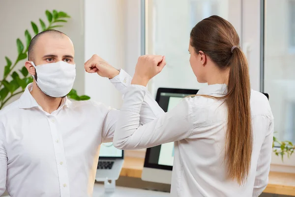 Elbow greeting to avoid the spread of coronavirus (COVID-19). A man with a medical face mask and a girl meet in an office with bare hands. Instead of greeting with a hug or handshake, they bump elbows