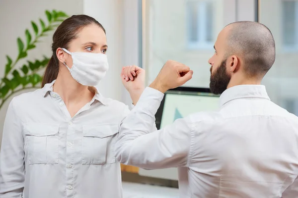 Elbow greeting to avoid the spread of coronavirus (2019-nCoV). Girl with a medical face mask and man meet in an office with bare hands. Instead of greeting with a hug or handshake, they bump elbows