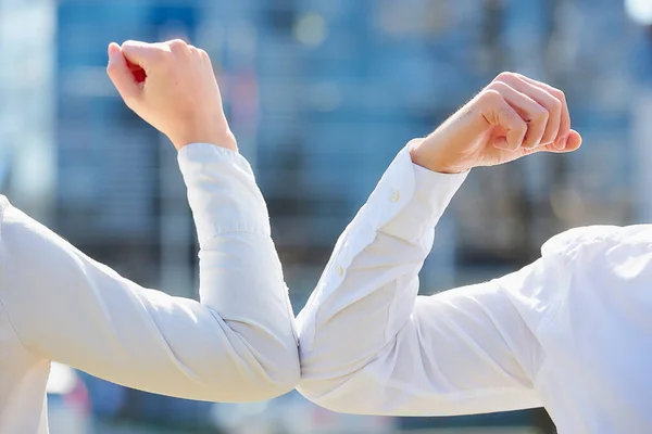 Elbow bumping. Elbow greeting to avoid the spread of coronavirus (COVID-19). Colleagues in shirts meet in the street with bare hands. Instead of greeting with hug or handshake, they bump elbows.