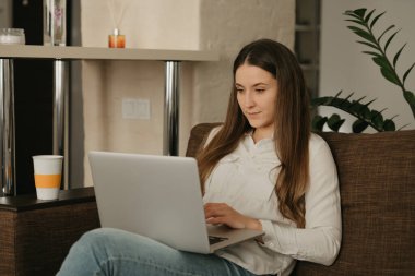 Uzaktan kumanda. Laptopuyla uzaktan çalışan beyaz bir kadın var. Kanepede evden çalışan bir iş kadını..
