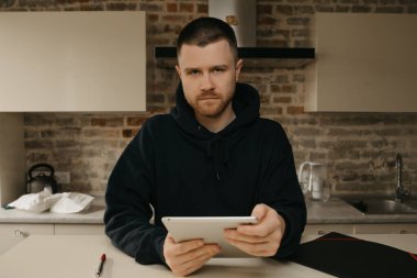 Uzaktan kumanda. Tabletinin üzerinde uzaktan çalışan sakallı bir adam. Evde iş yapan bir adam..