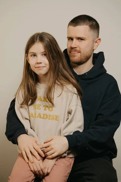 A young happy dad with a beard fooling around with his pretty daughter. A child with long hair sitting on daddy\'s lap. Family photo.