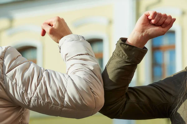 Elbow bumping. Elbow greeting to avoid the spread of coronavirus (COVID-19). Friends bump elbows to each other instead of greeting with a handshake or hug in the background of windows of an old house.