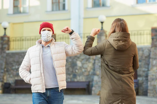 Elbow bumping. Elbow greeting to avoid the spread of coronavirus (COVID-19). A woman and a man in medical face masks bump elbows instead of greeting with a hug or handshake in the old town.