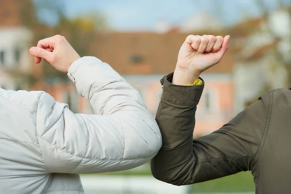 A close-up photo of elbow bumping. Elbow greeting to avoid the spread of coronavirus (COVID-19). A woman and man in medical masks bump elbows instead of greeting with hug or handshake in the old town.