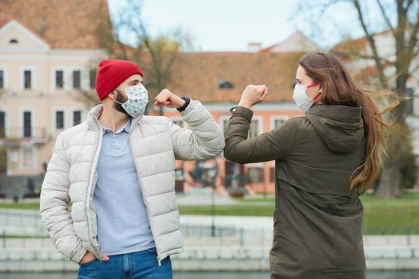 Elbow bumping. Elbow greeting to avoid the spread of coronavirus (COVID-19). A man with a beard and a woman with long hair in medical masks bump elbows instead of greeting with a hug or handshake.