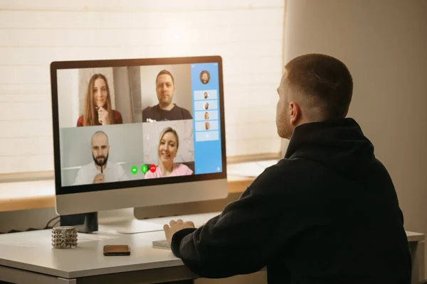 Remote work. A back view of a man during a video call with his colleagues on the desktop computer. A fellow on an online briefing working from home.