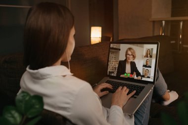 Bir kadının evinde kanepeye uzanmış patronuyla ve diğer iş arkadaşlarıyla dizüstü bilgisayardaki bir video görüşmesinde konuşmasının arkası. İş kadını web kamerası konferansında iş arkadaşlarıyla konuşuyor. Toplantı yapan bir takım..