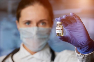 Kadın bir bulaşıcı hastalık doktoru, tek kullanımlık bir tıbbi eldivenin içinde beyaz önlük ve tıbbi maske takar ve Coronavirus (COVID-19) aşısı yapar. Hastanede aşısı olan bir doktor.. 