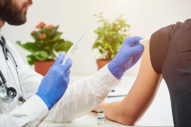 Tek kullanımlık tıbbi eldivenleri olan bir erkek doktor, ofisindeki hastaya koronavirüs aşısı yapmaya hazırlanıyor. Bir hastanede COVID-19 aşısı kullanan bulaşıcı bir doktor.. 