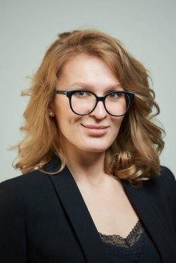 Siyah takım elbiseli, siyah gömlekli, gözlüklü şık bir genç kadın. İş kıyafeti giyen ve gülümseyen sarışın bir bayanın yakın plan portresi. Ofis tarzı bir gardırop..