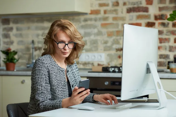 A woman in glasses works remotely on a desktop computer in her studio. A boss distracted by a smartphone during a video conference at home. A professor uses a cellphone before an online lecture.