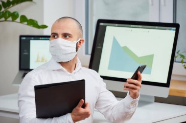 Virüse karşı koruyucu maske takan bir adam. 2019-NCoV 'a karşı cerrahi maskeli bir doktor dikkati telefondan dağılmış ve diğer elinde de ofisinde bir dosya var. Coronavirus karantinası.