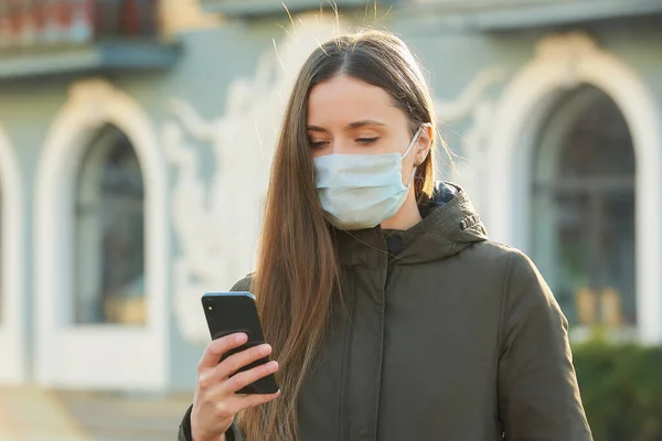 A woman using a smartphone wears a medical face mask to avoid the spread coronavirus on a street. A girl with a surgical mask on the face against COVID-19