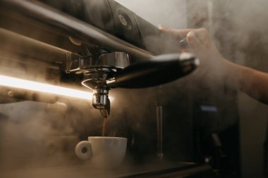 Profesyonel bir kahve makinesinin yakın bir fotoğrafı. Kahveci kahve makinesinden beyaz fincana espresso döker. Buharla..