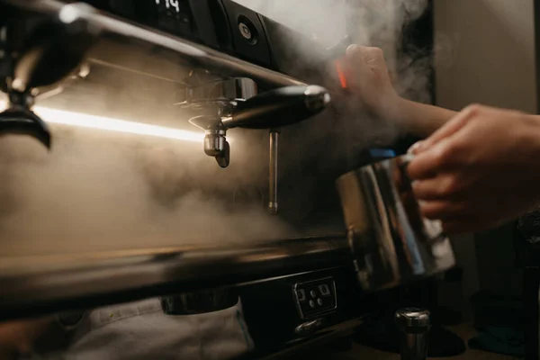 A close photo of a professional coffee machine. A barista steams a metal mug.