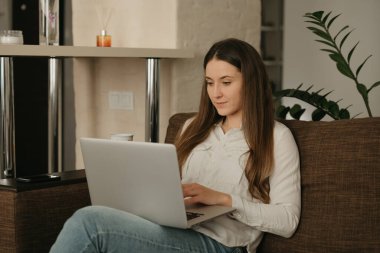 Uzaktan kumanda. Laptopuyla uzaktan çalışan beyaz bir kadın var. Kanepede evden çalışan bir iş kadını..