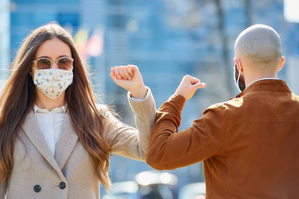 Elbow bumping. Elbow greeting to avoid the spread of coronavirus (COVID-19). Man and woman in the sunglasses meet in the street with bare hands. Instead of greeting with a hug or handshake, they bump elbows.