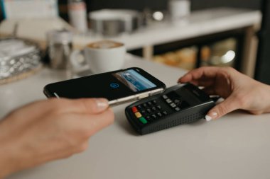 Kahvesini akıllı telefonuyla ödeyen bir kadın bir kafede parasız servis teknolojisiyle bağlantı kuruyor. Bayan bir barista müşteriye ödeme yapmak için terminali soyar..