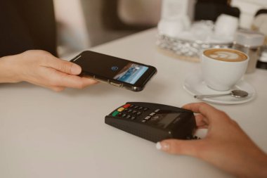 Kahvesini akıllı telefonla ödeyen bir kadın bir kafede NFC teknolojisiyle temas kuramıyor. Kadın bir barista, bir kahve dükkanında müşteriye ödeme yapmak için bir terminali soyar..
