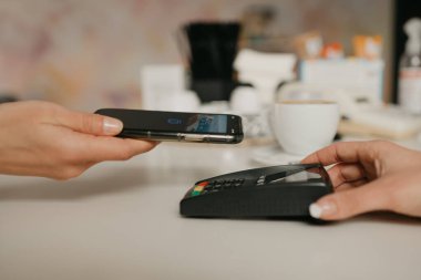 Bir kafedeki NFC teknolojisiyle akıllı telefonuyla kahvesini ödemeye hazırlanan bir kadın. Kadın bir barista, bir kahve dükkanında müşteriye ödeme yapmak için bir terminali soyar..