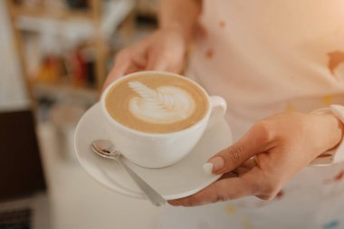 Kahve dükkanında bayan bir baristanın elinde tuttuğu bir fincan kahvenin yakın plan fotoğrafı. Kahveci kafede sipariş hazırlıyor..