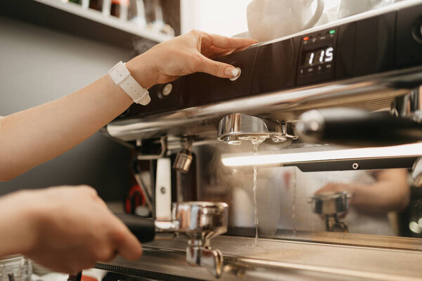 A female barista purging a grouphead thoroughly with hot water in the espresso machine in a coffee shop. A barista cleaning in a cafe.