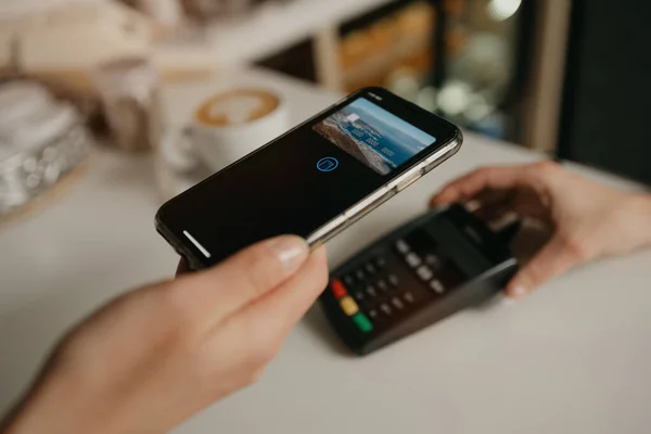 一位女士在咖啡店用智能手机用无接触式付费电话支付她的拿铁费用 一位女酒保在咖啡店里摆设了一个终端 为顾客付款 — 图库照片