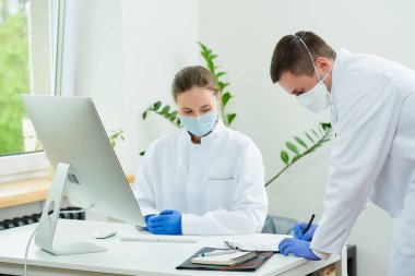 Tıbbi maskeli bir cerrah ve radyoloji uzmanı hastanede bir hastanın analizini tartışıyor. Masaüstü bilgisayarının önünde oturan bir kadın doktor. Yanında bir terapist oturuyor..