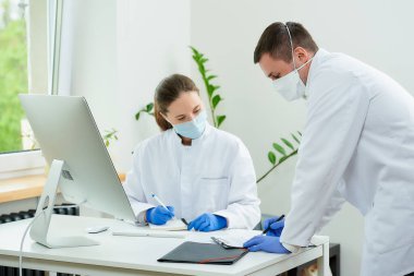 Tıbbi maskeli bir cerrah ve radyoloji uzmanı hastanede yatan bir hastaya teşhis koyuyor. Masaüstü bilgisayarının önünde oturan bir kadın doktor. Yanında bir terapist oturuyor..