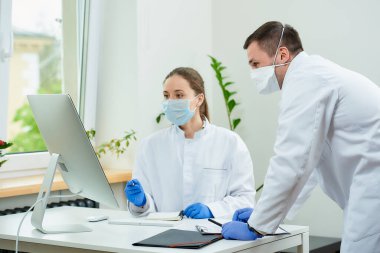 Tıbbi maskeli bir cerrah ve radyoloji uzmanı masaüstü bilgisayarında bir hastanın teşhisini tartışıyor. Bilgisayarın önünde oturan bir kadın doktor, yanında bir terapist oturuyor..