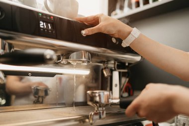 Kahve makinesindeki sıcak suyla grup liderini iyice temizleyen bir bayan barista. Kafede temizlik yapan bir barmen..