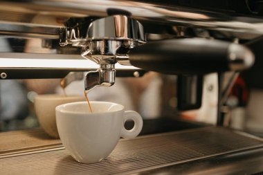 Kahve dükkanında profesyonel bir espresso makinesinde Espresso demlemek. Kafedeki kahve makinesinden beyaz bir fincana dökülen kahvenin yakın çekimi..