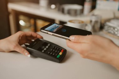 Kahvesini akıllı telefonla ödeyen bir kadın bir kafede parasız satış teknolojisi kullanıyor. Kadın bir barista, bir kahve dükkanında müşteriye ödeme yapmak için bir terminali soyar..