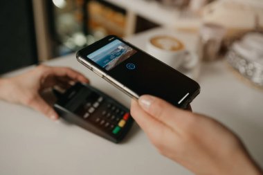 Kahvesini akıllı telefonuyla ödeyen bir bayan bir kafede parasız servis teknolojisiyle iletişim kuruyor. Kadın bir barista, bir kahve dükkanında müşteriye ödeme yapmak için bir terminali soyar..