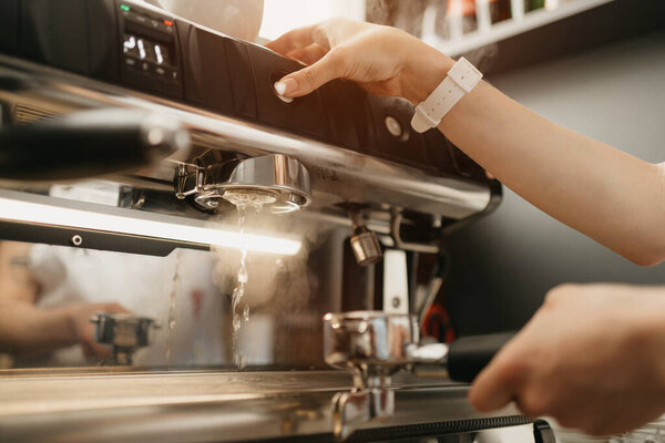 A female barista purging a grouphead thoroughly with hot water in the espresso machine in a coffee shop. A barista works in a cafe.