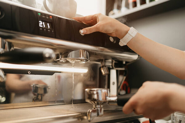 A female barista purging a grouphead thoroughly with hot water in the espresso machine in a coffee shop. A barista cleaning in a cafe.