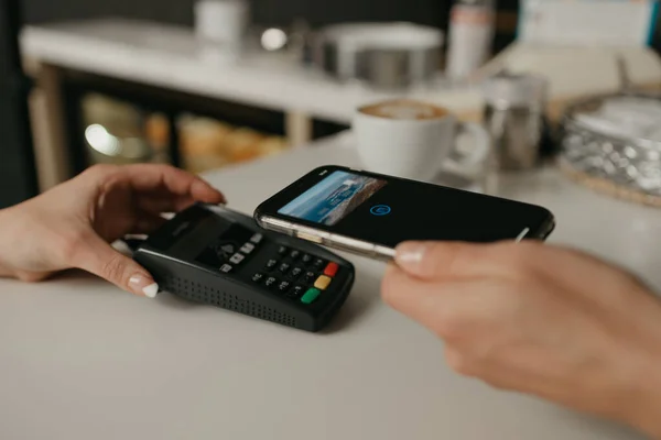 Kahvesini akıllı telefonuyla ödeyen bir kadın bir kafede parasız servis teknolojisiyle bağlantı kuruyor. Bayan bir barista müşteriye ödeme yapmak için terminali soyar..