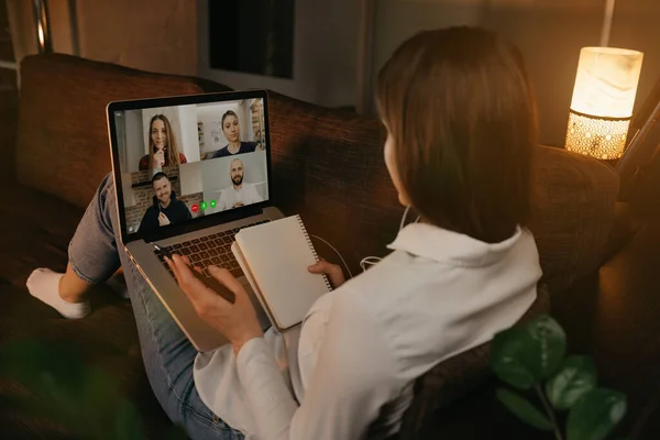 Bir kadının evinde kanepeye uzanmış iş arkadaşlarıyla dizüstü bilgisayardaki bir video görüşmesinde konuşmasının arkası. İş kadını, video konferansı sırasında not defterine not tutuyor. Çevrimiçi toplantı yapan bir takım.