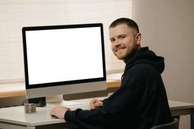 Remote work. A businessman works remotely using an all-in-one computer. A smiling fellow with a beard working from home.  clipart
