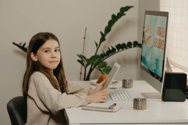 Distance learning. A young girl with long hair studying remotely online. A happy female child learns a lesson using an all-in-one computer at home. Home education. clipart