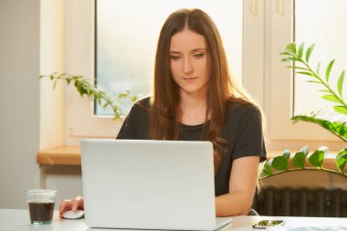Karantina sırasında Coronavirus 'un yayılmasını önlemek için dizüstü bilgisayarıyla uzaktan çalışan beyaz bir kadın. COVID-19 salgını sırasında akşamları evden çalışan bir iş kadını..